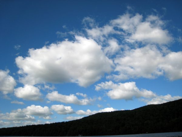 Blue sky with fluffy white clouds over a shadowed hill