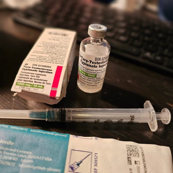 Box and bottle of taro-testosterone cypionate, a syringe and its packaging on a desk. Photo by Nico Mara-McKay.