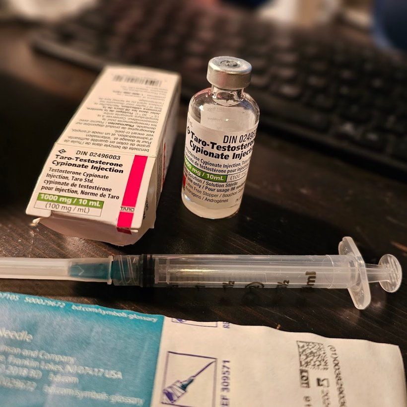 Box and bottle of taro-testosterone cypionate, a syringe and its packaging on a desk. Photo by Nico Mara-McKay.