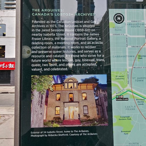 The pillar reads, "Founded as the Canadian Lesbian and Gay Archives in 1973, The ArQuives is situated in Jared Sessions House (1859-60) on nearby Isabella Street. It contains the James Fraser Library, the National Portrait Gallery, a reading room, a meeting room, and an eclectic collection of materials. It works to recover and preserve queer histories, and serves as a resource and catalyst for those who strive for a future where lesbian, gay, bisexual, trans, queer, two spirit, and others are accepted, valued, and celebrated. Followed by a photo of the building with a caption noting its location and the photographer." Photo by Nico Mara-McKay.